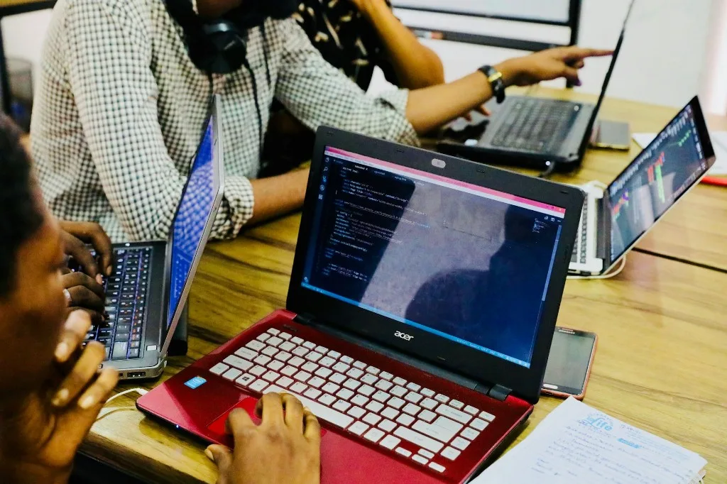 Developers collaborating on laptops with code on screen in a modern workspace